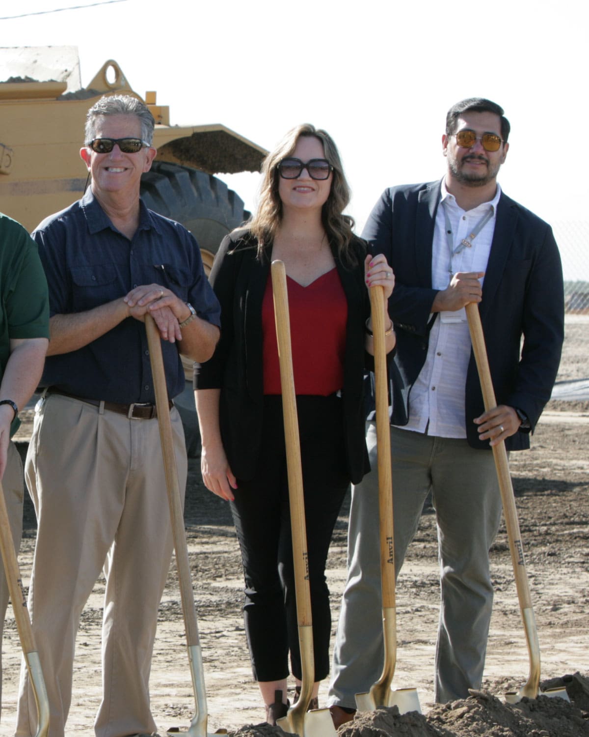 Three Teter employees holding shovels and smiling at a construction groundbreaking site, with heavy equipment in the background.