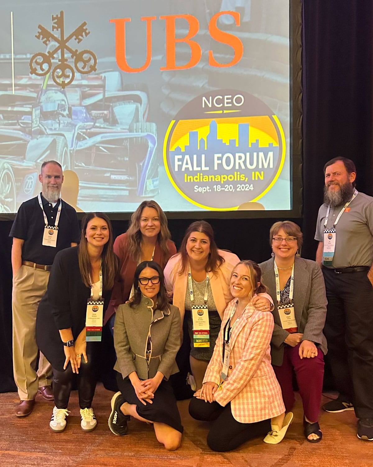 A group of Teter employees at the NCEO Fall Forum in Indianapolis, gathered under a screen displaying event logos and smiling proudly.