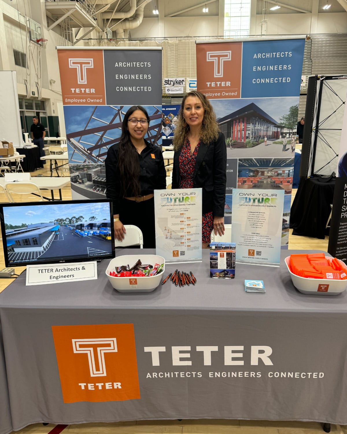 Two Teter employees standing behind a career fair booth displaying company banners, brochures, and branded items.