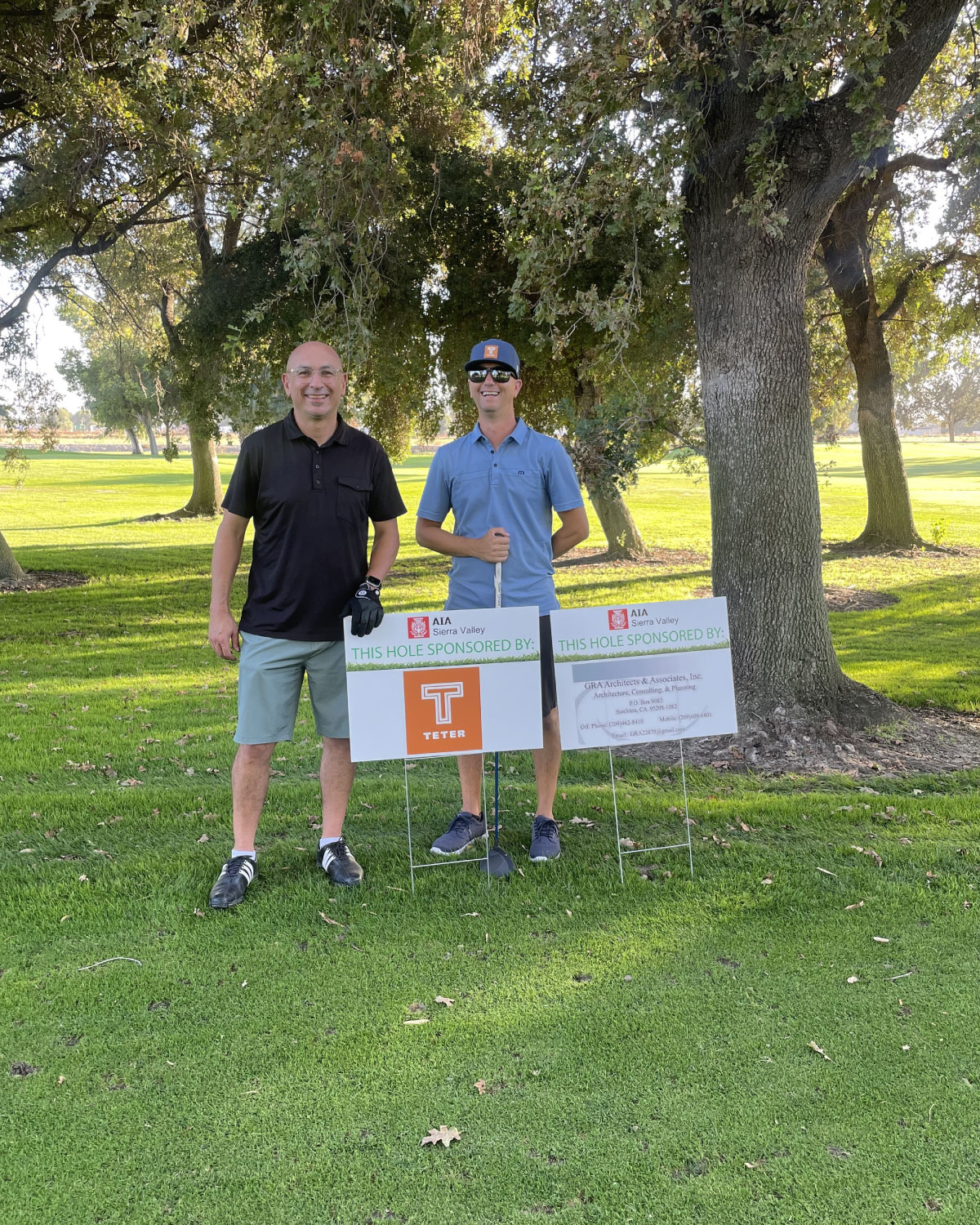 Two Teter employees posing on a golf course next to a sign indicating Teter’s sponsorship of the hole.