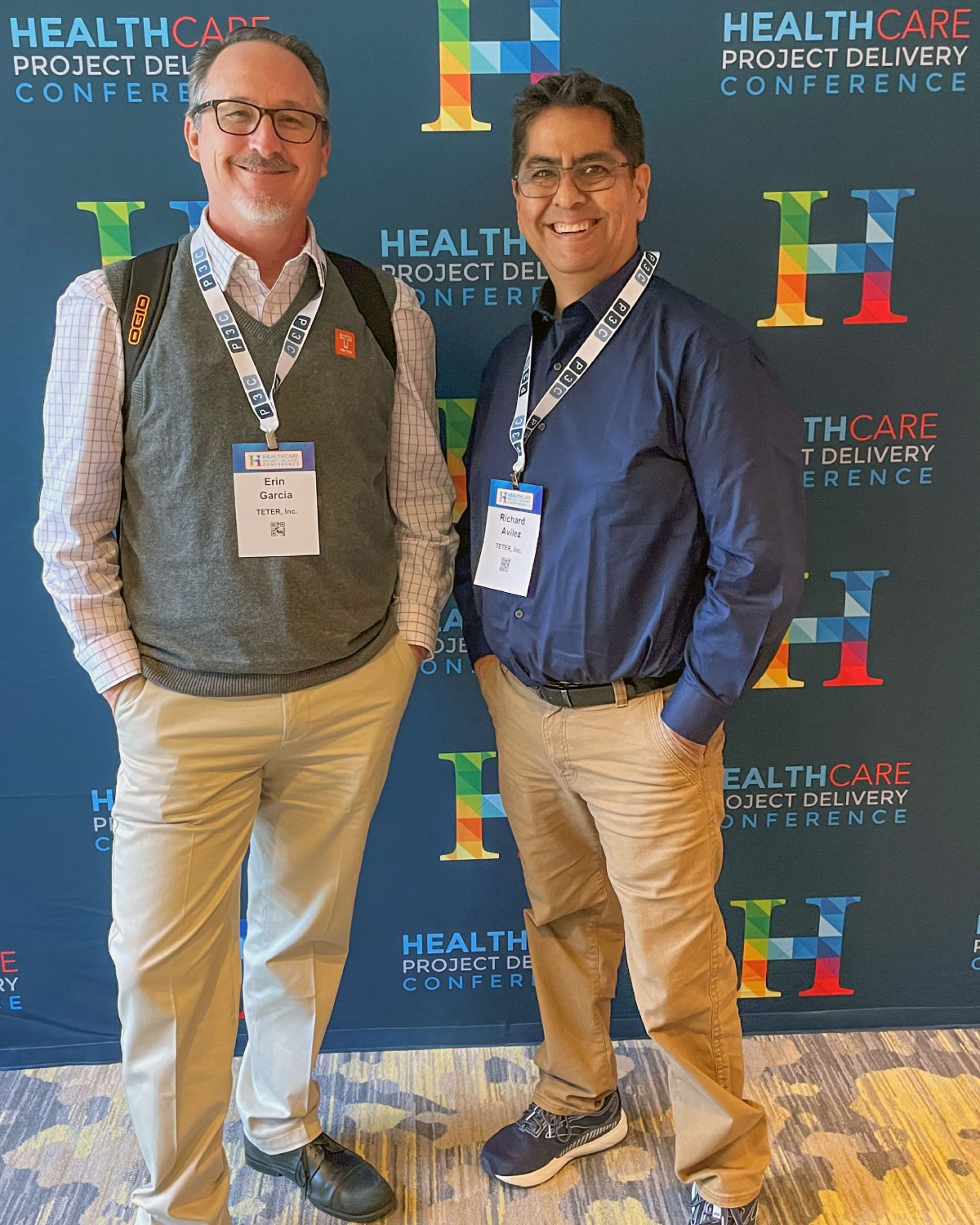 Two Teter employees smiling in front of a Healthcare Project Delivery Conference backdrop.