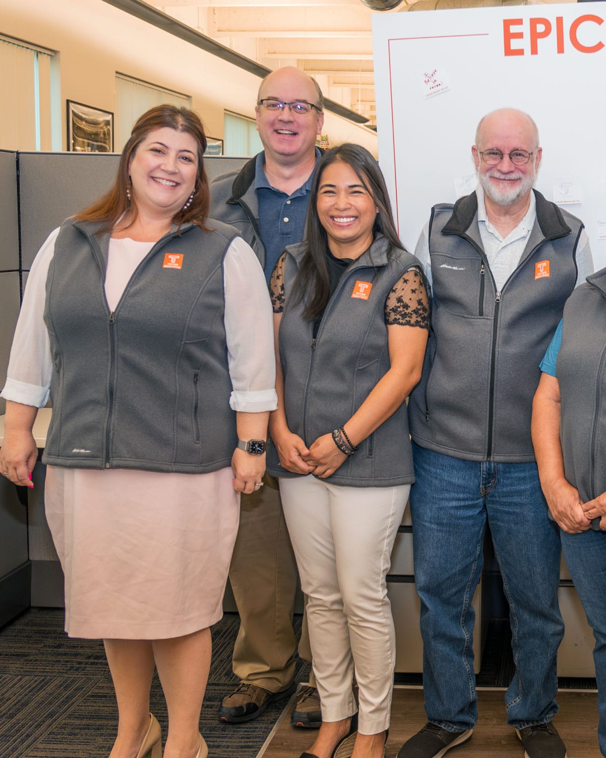 A group of Teter employees wearing matching branded vests, smiling together inside an office setting.