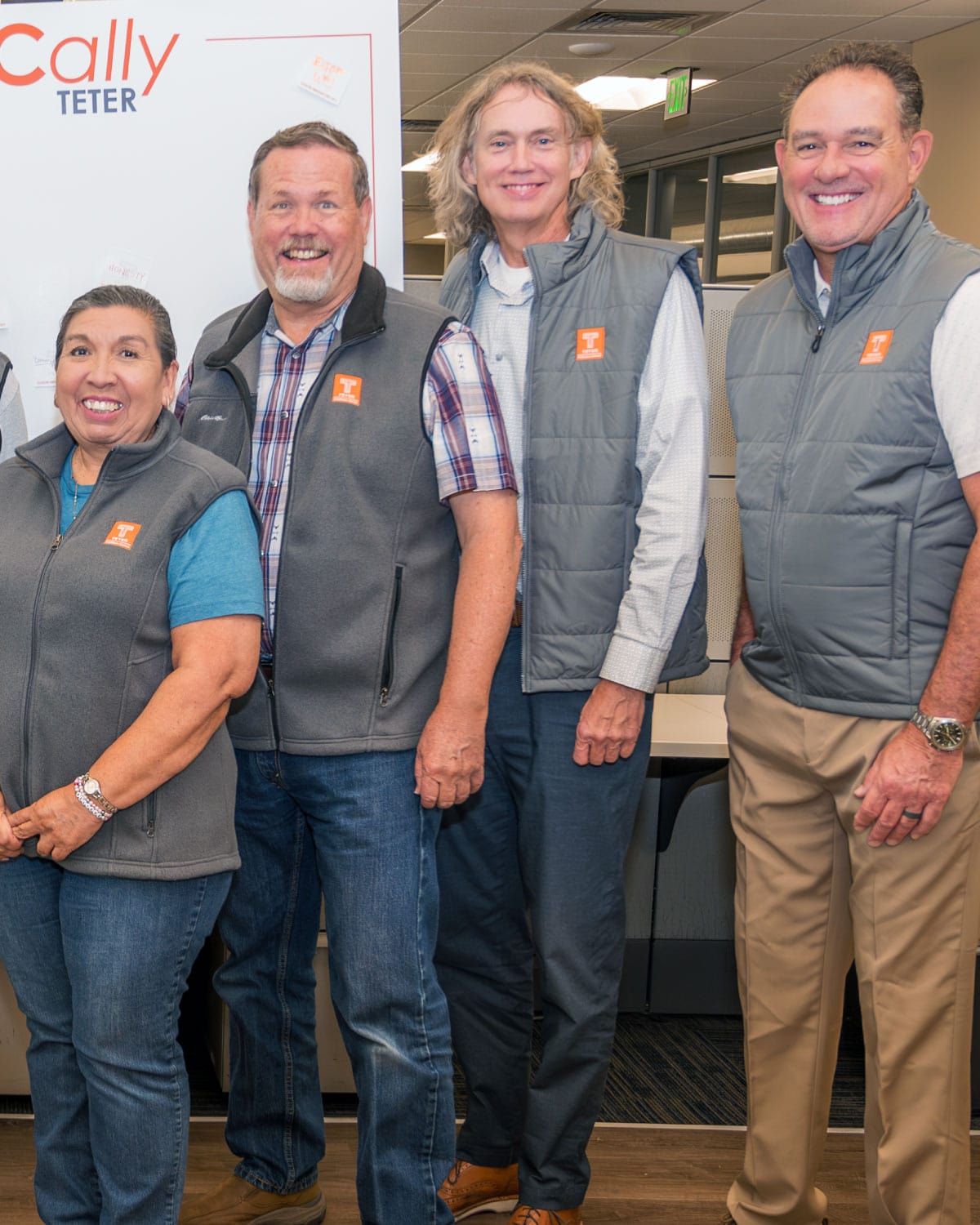 A group of Teter employees wearing matching branded vests, smiling together inside an office setting.