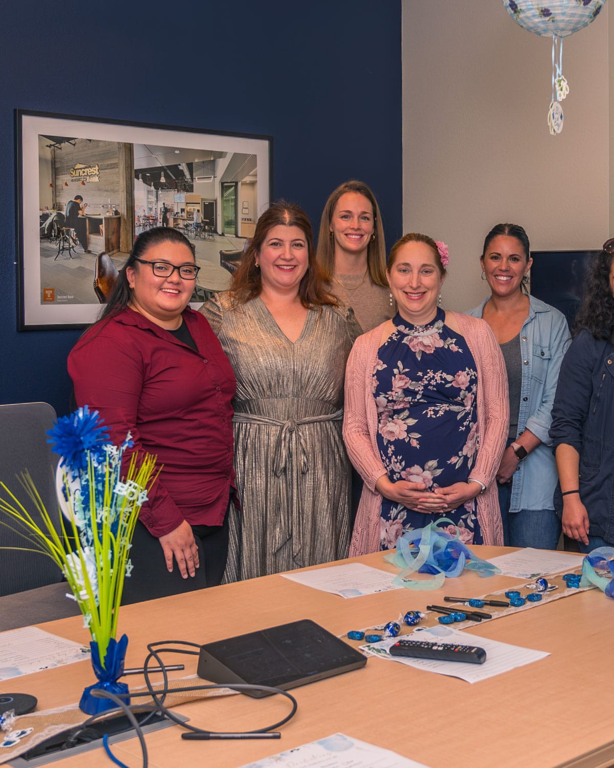 A group of Teter employees gathered around a decorated table indoors, smiling together during a celebratory event.