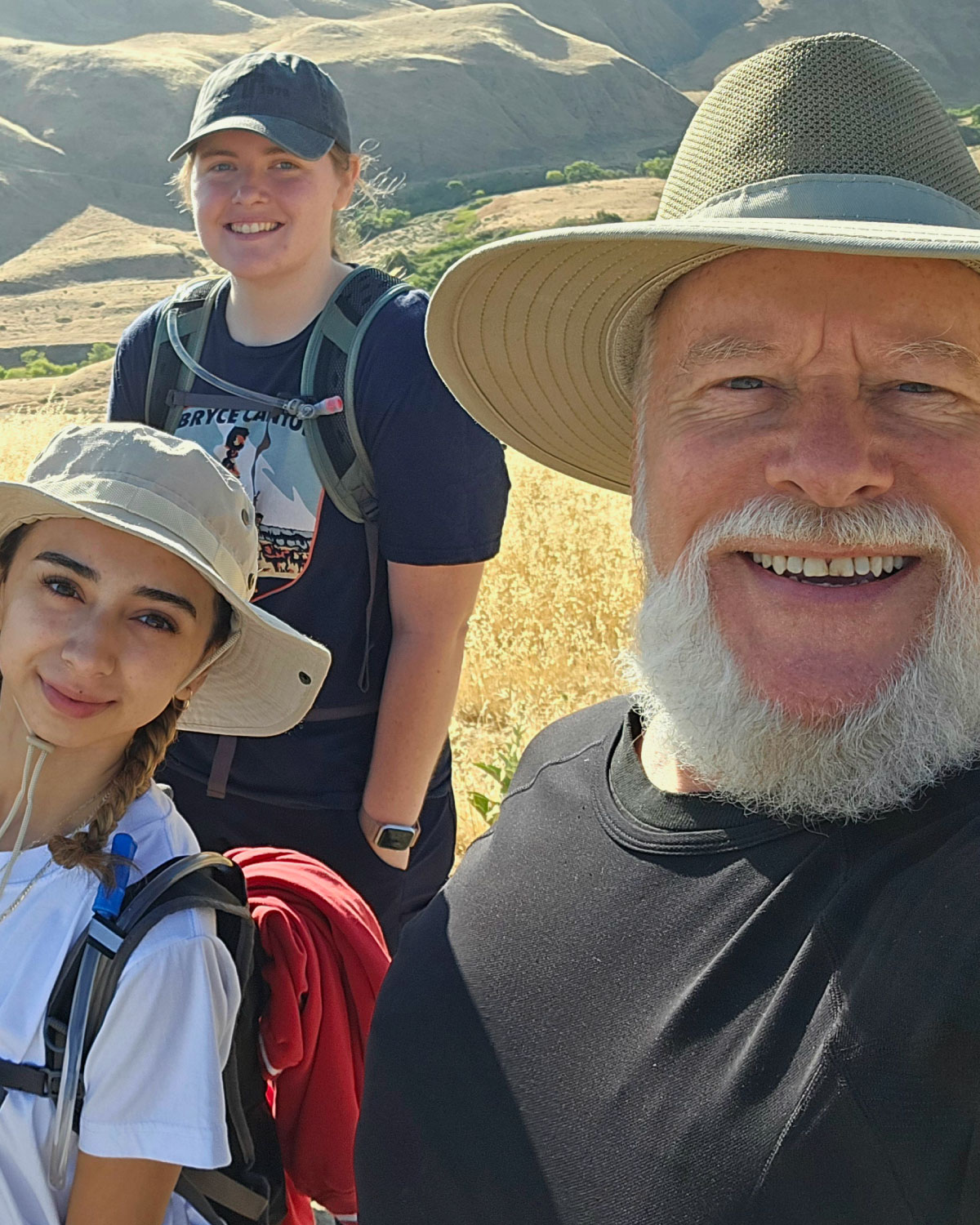 A group of Teter employees wearing outdoor gear, smiling and standing together on a hiking trail with rolling hills in the background.