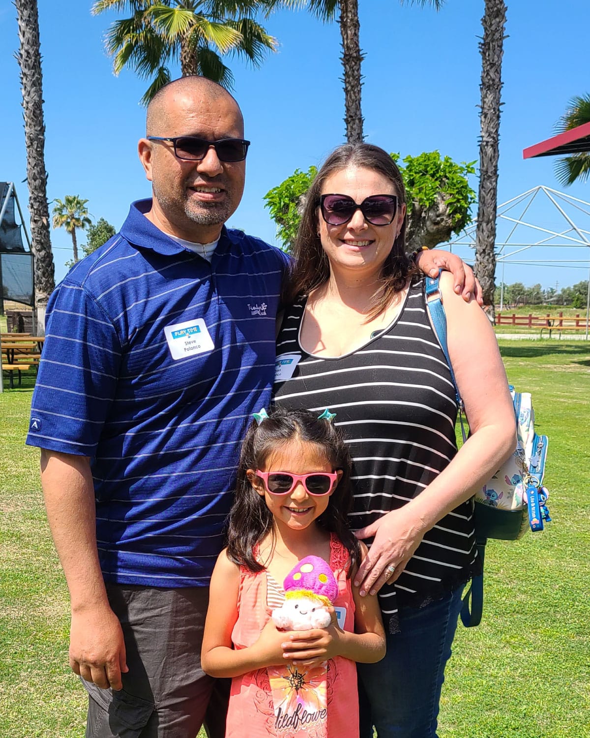 A Teter employee with their family, including a young child in pink sunglasses, smiling outdoors under palm trees.