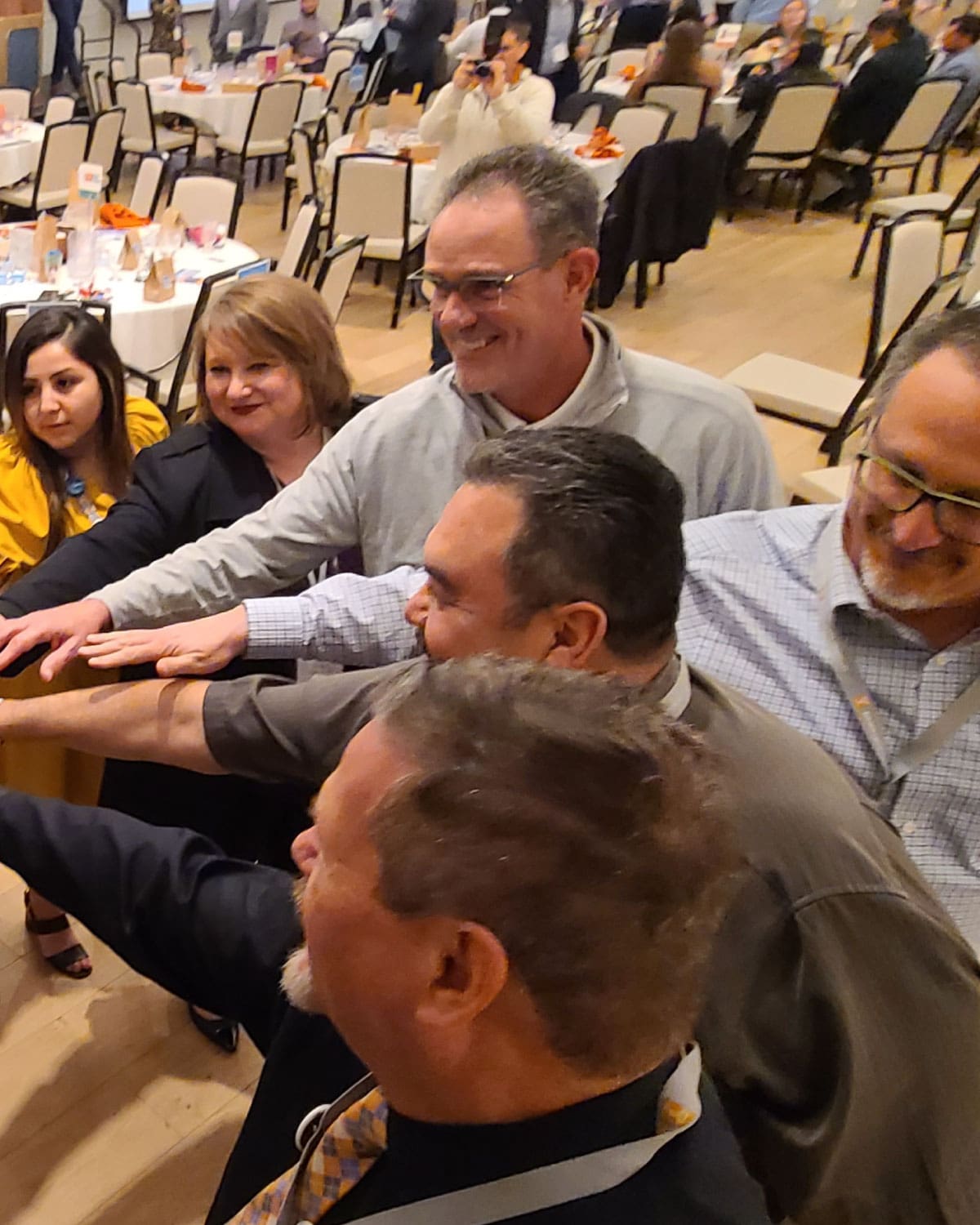 A group of Teter employees standing in a circle, reaching their hands inward for a unified team gesture at an indoor event.