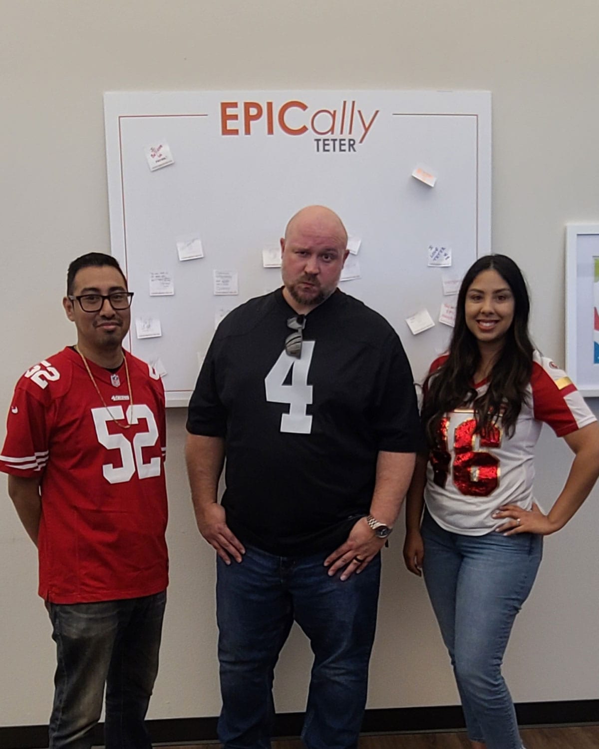 Three Teter employees wearing football jerseys, posing in front of an ‘EPICally TETER’ board.