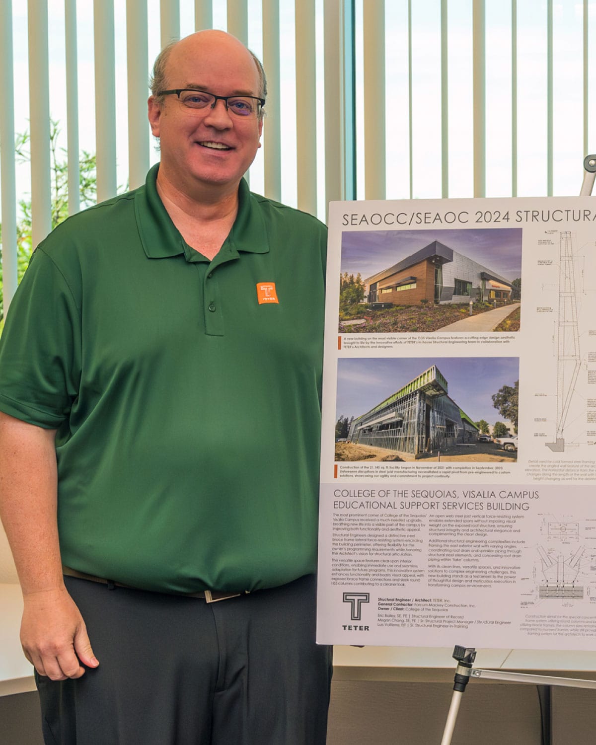 A Teter employee in a green polo shirt smiling beside a structural engineering project board.