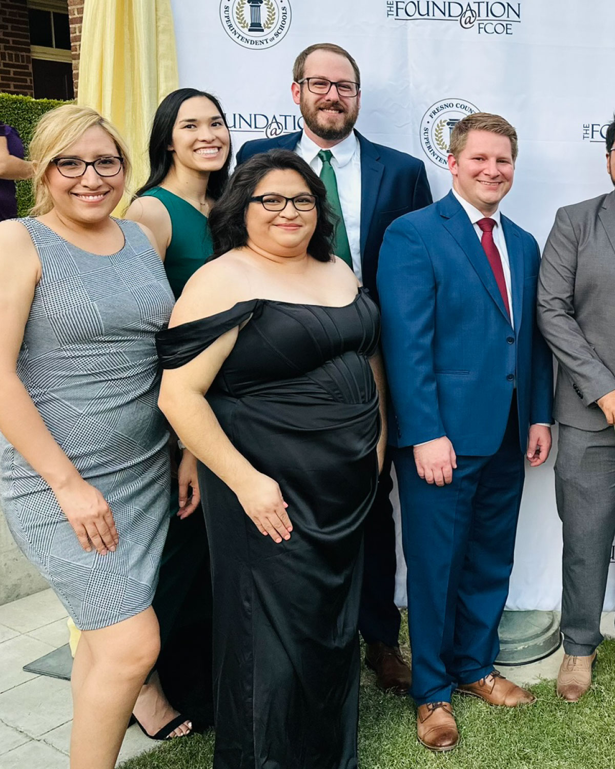 A group of Teter employees dressed in formal attire smiling together in front of a ‘The Foundation at FCOE’ event backdrop.